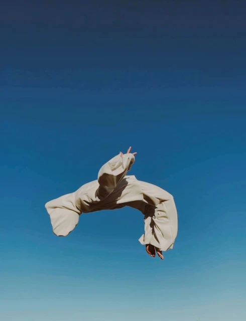 Artistic studio shot of a person in a flowing beige outfit mid-jump against a clear blue sky backdrop on a sunny day.  