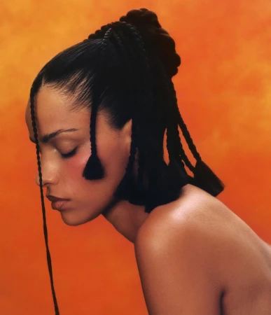 Profile portrait of a woman with braided updo hairstyle against a vibrant orange textured backdrop photographed by Julia Grandperret
