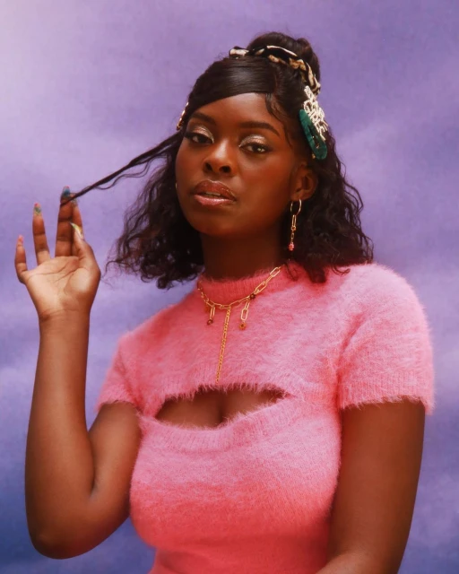Portrait of an African American woman with a pink top and jewelry against a lavender background in a studio fashion shot.