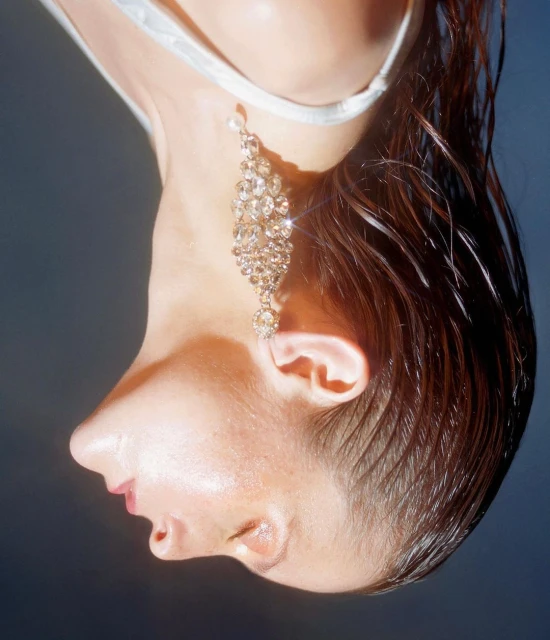 Close-up of a woman's profile wearing a chandelier earring; the image is vertically inverted, showcasing beauty and wet hair.