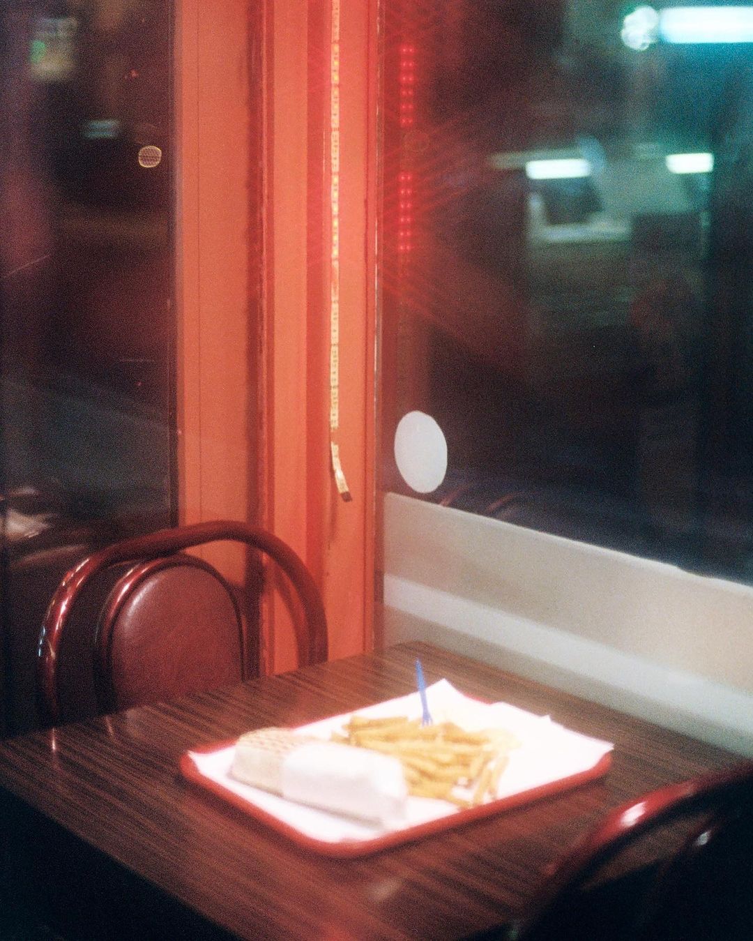 Diner table with fries and a wrap, illuminated by warm indoor lighting and viewed through a restaurant window at nighttime.