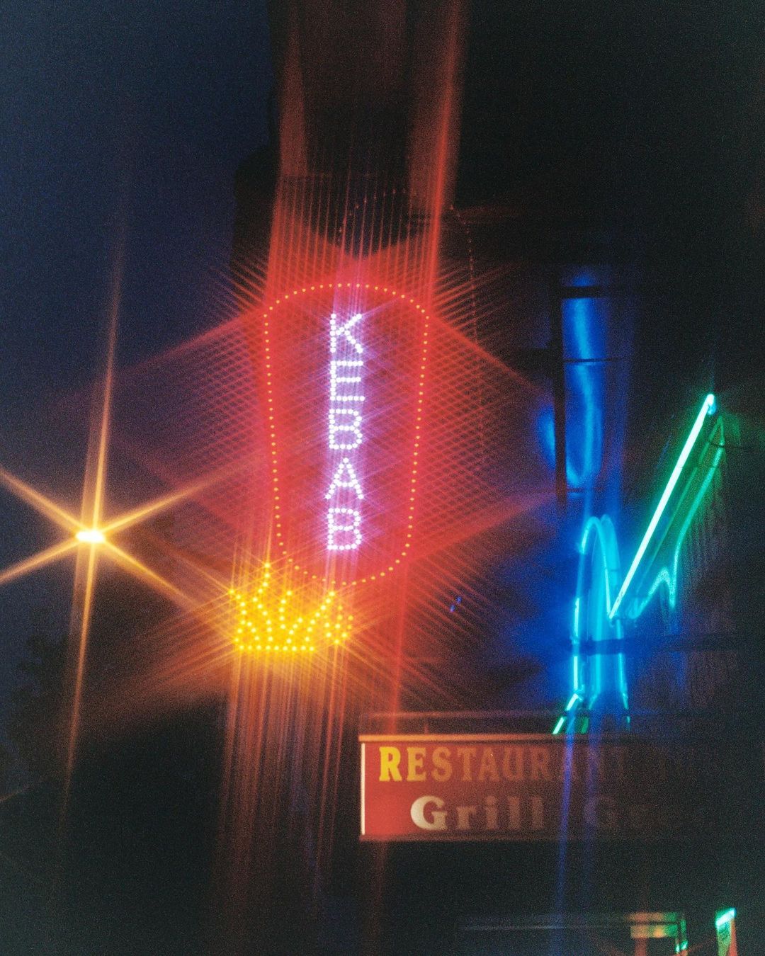 Nighttime photograph of a restaurant's neon sign that advertises 'Kebab'. Starbursts from the streetlights add to the urban feel.