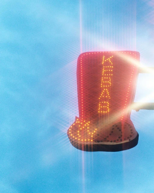 Illuminated kebab restaurant sign against a light blue sky. Vertical red and yellow text and pattern shape for advertising food.