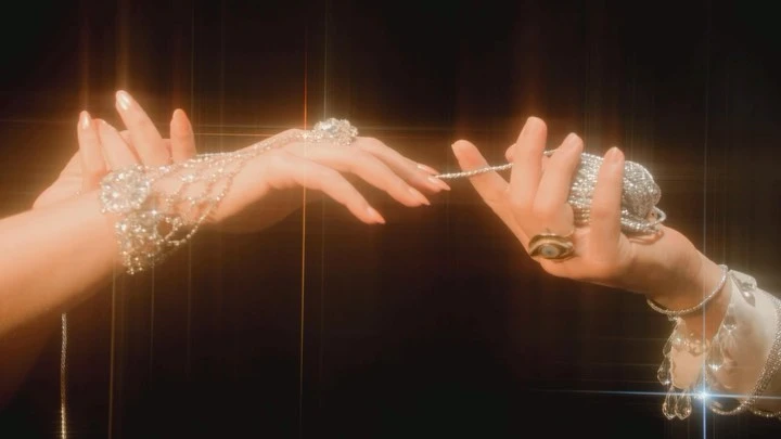 Close-up studio shot featuring two hands adorned with elaborate jewelry, including rings and bracelets, against a dark backdrop.