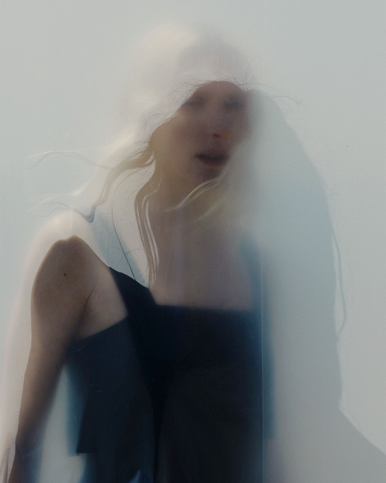 Woman in a black dress behind a semi-transparent white veil, portrait shot, studio lighting.