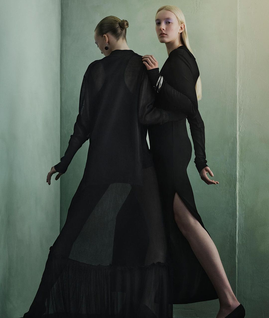 Two models in black dresses posing against a muted green wall in a portrait captured by photographer Julia Hetta.