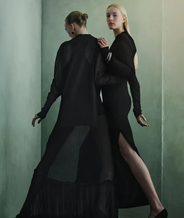 Two models in black dresses posing against a muted green wall in a portrait captured by photographer Julia Hetta.