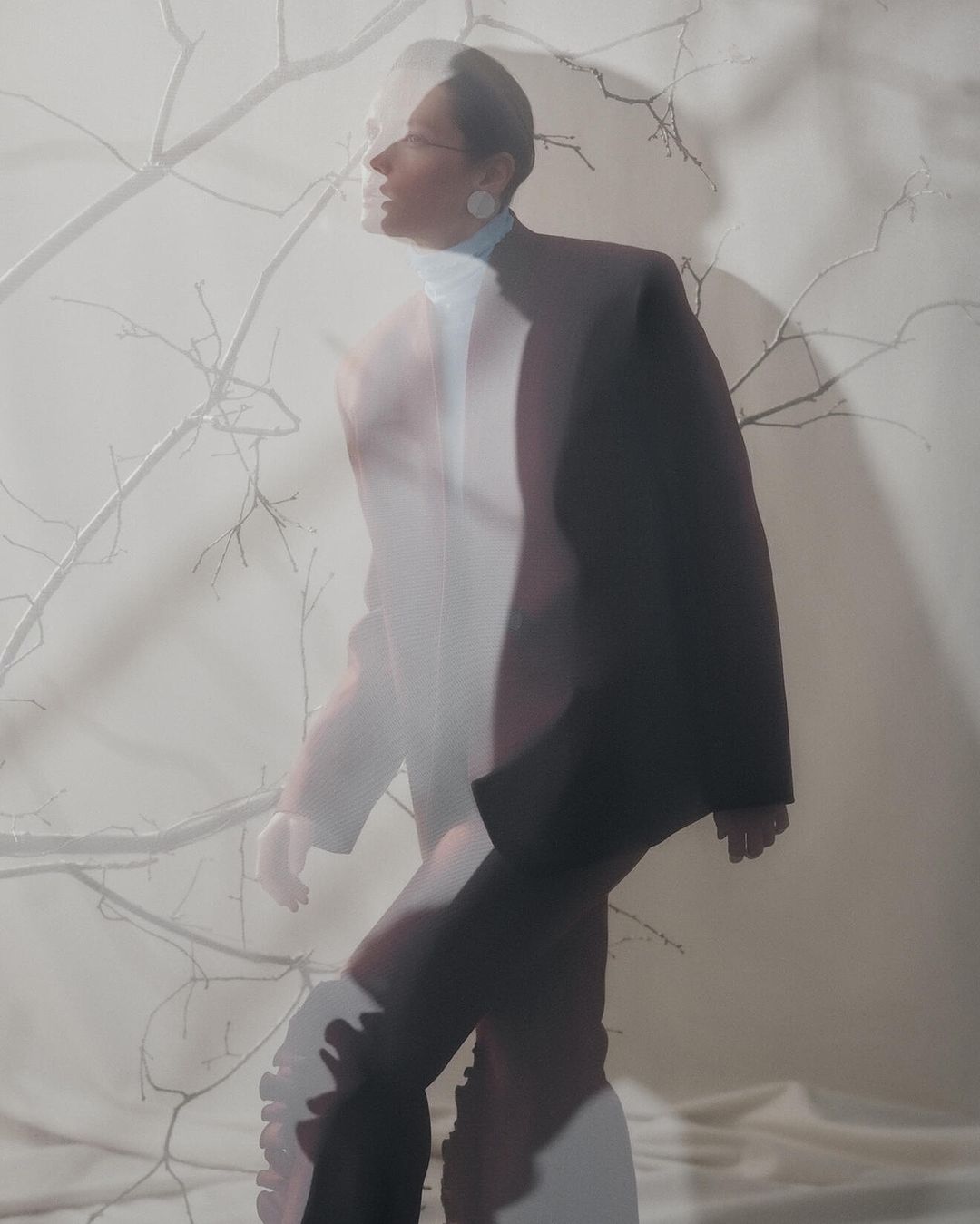 Portrait of a model in a dark blazer with multiple exposure effect against a pale background with bare tree branches