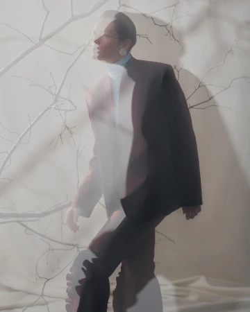 Portrait of a model in a dark blazer with multiple exposure effect against a pale background with bare tree branches