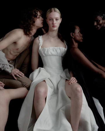 Group of four models posing in dark atmospheric lighting, centered on a woman in a white dress