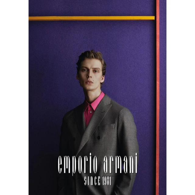 Man in a gray suit and pink shirt poses in front of a purple backdrop with a yellow and orange geometric accent; Emporio Armani logo.