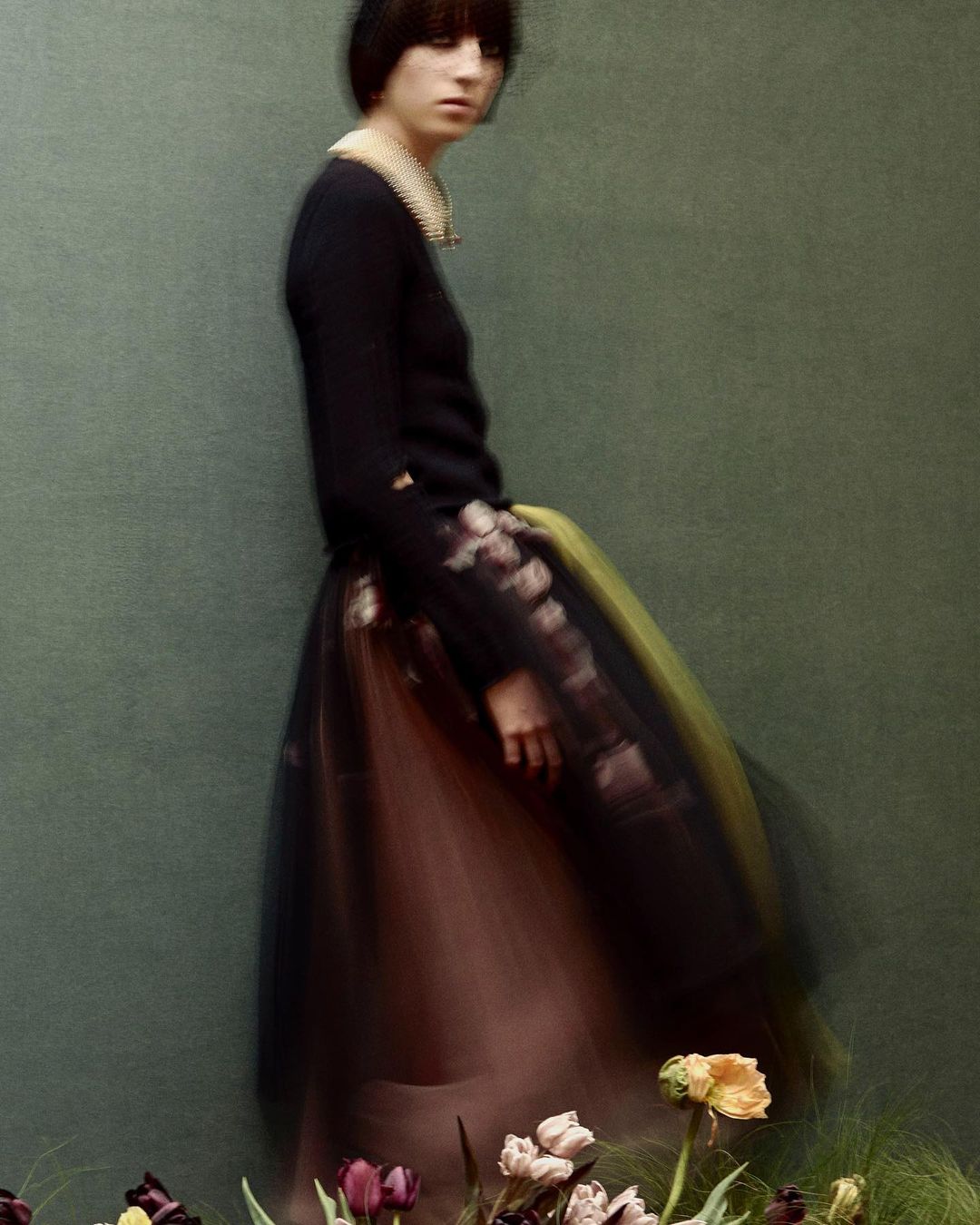 Model with dark bob hairstyle wearing a black top and layered tulle skirt behind flowers by Julia Hetta