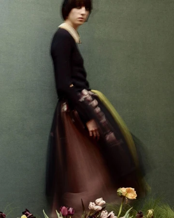 Model with dark bob hairstyle wearing a black top and layered tulle skirt behind flowers by Julia Hetta
