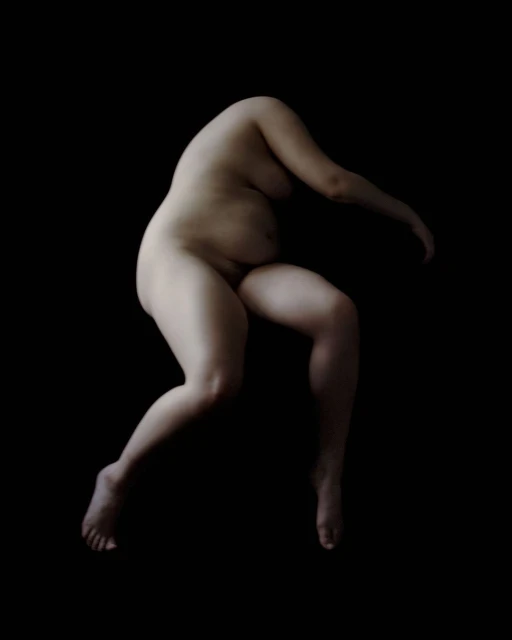 Nude female figure in a contorted pose against a stark black backdrop, lit with soft lighting, showing the natural curves of the body.