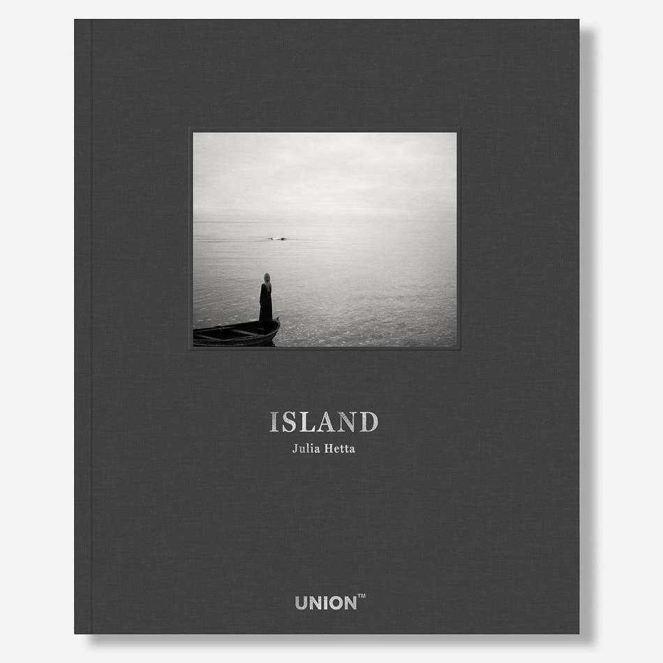 Book cover of 'Island' by Julia Hetta features a black and white image of a person on a boat in the ocean, under a gray sky.