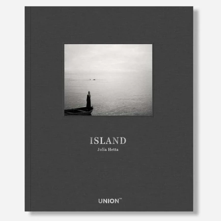 Book cover of 'Island' by Julia Hetta features a black and white image of a person on a boat in the ocean, under a gray sky.