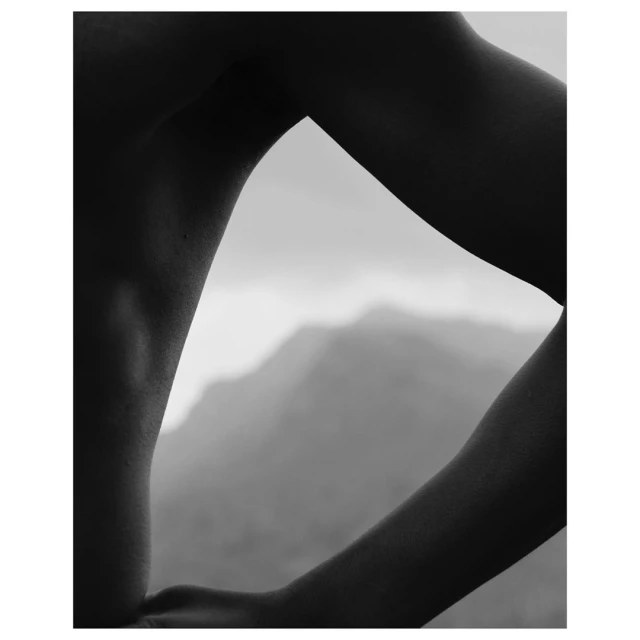 Black and white photograph featuring the arm and upper body of a person set against a blurred background landscape of a mountain range.