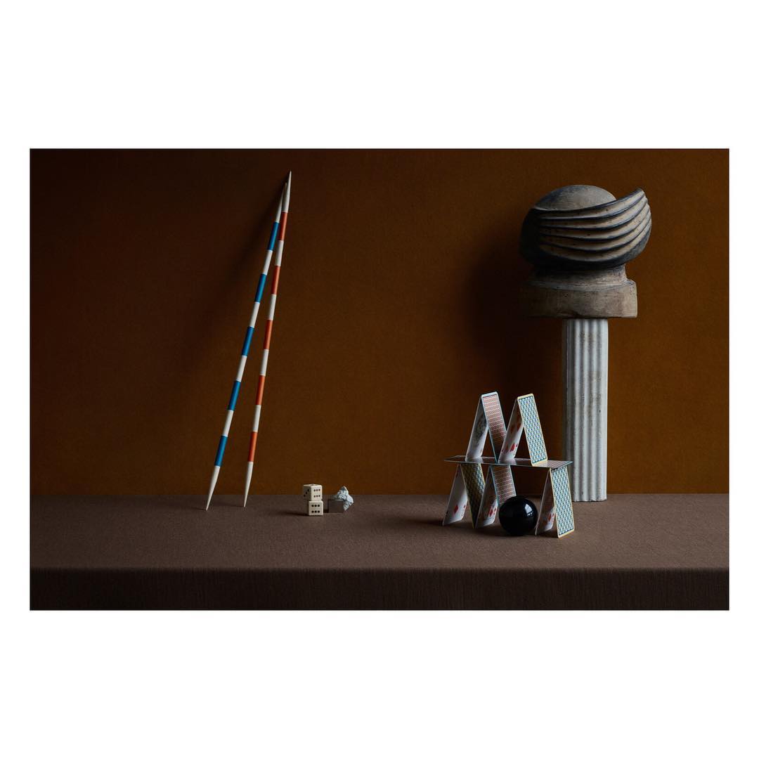 Still life shot of a house of cards with dice and Mikado sticks on a brown surface, set against a dark brown background.