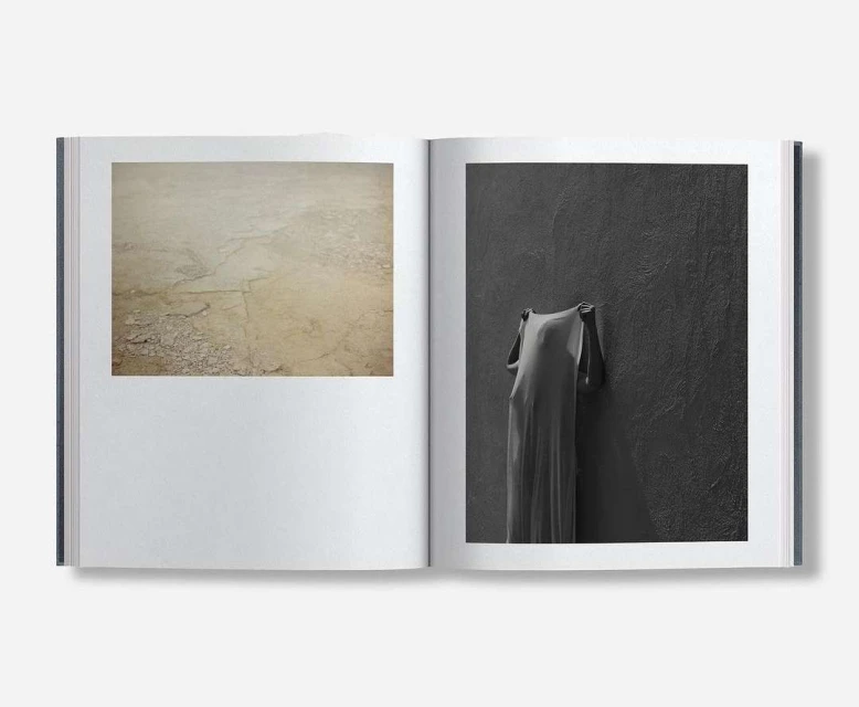 Open book displays a photograph of sandy terrain and an image of a draped figure against a dark wall, inviting contemplation.