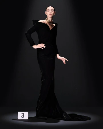 Elegant woman in a long black gown poses in a spotlight with a gold necklace, fashion forward, artistic studio shot.