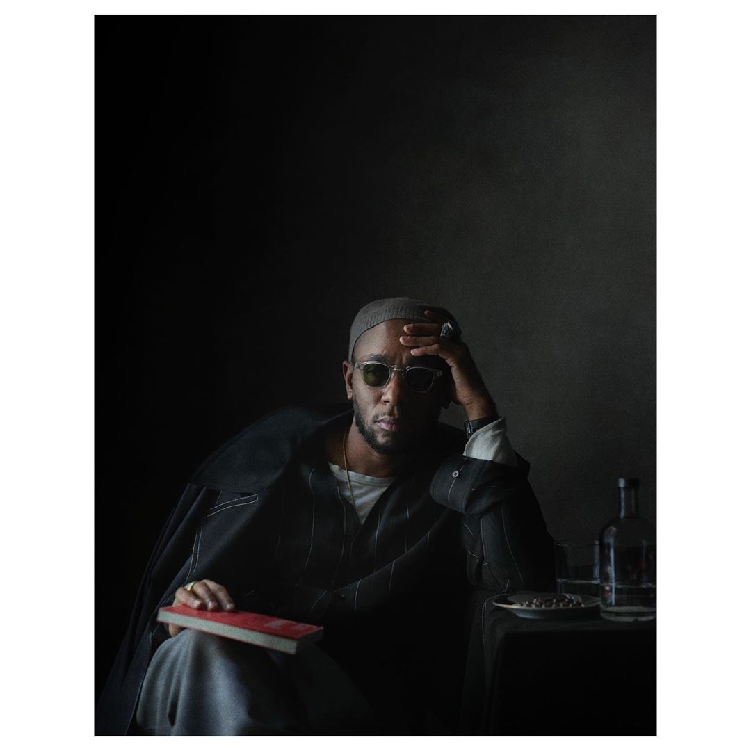 Portrait of a man wearing sunglasses, a beanie, and a dark jacket while holding a book by Julia Hetta