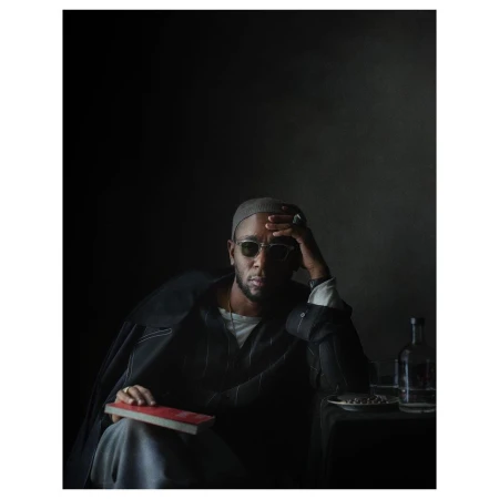 Portrait of a man wearing sunglasses, a beanie, and a dark jacket while holding a book by Julia Hetta