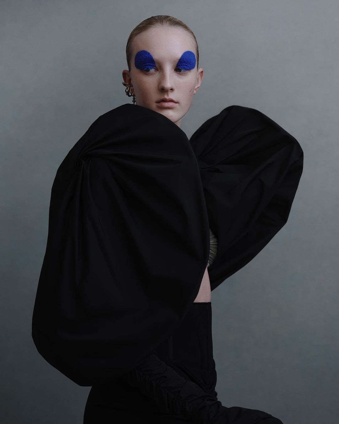 Model with slicked hair and bold blue eye makeup wearing an exaggerated black puffed sleeve top photographed by Julia Hetta