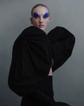 Model with slicked hair and bold blue eye makeup wearing an exaggerated black puffed sleeve top photographed by Julia Hetta