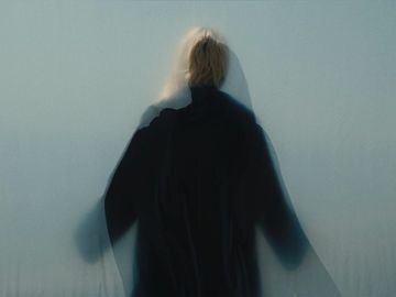 Abstract, blurred photo of person in dark clothing against a light background. Soft lighting and hazy effect.