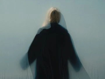 Abstract, blurred photo of person in dark clothing against a light background. Soft lighting and hazy effect.