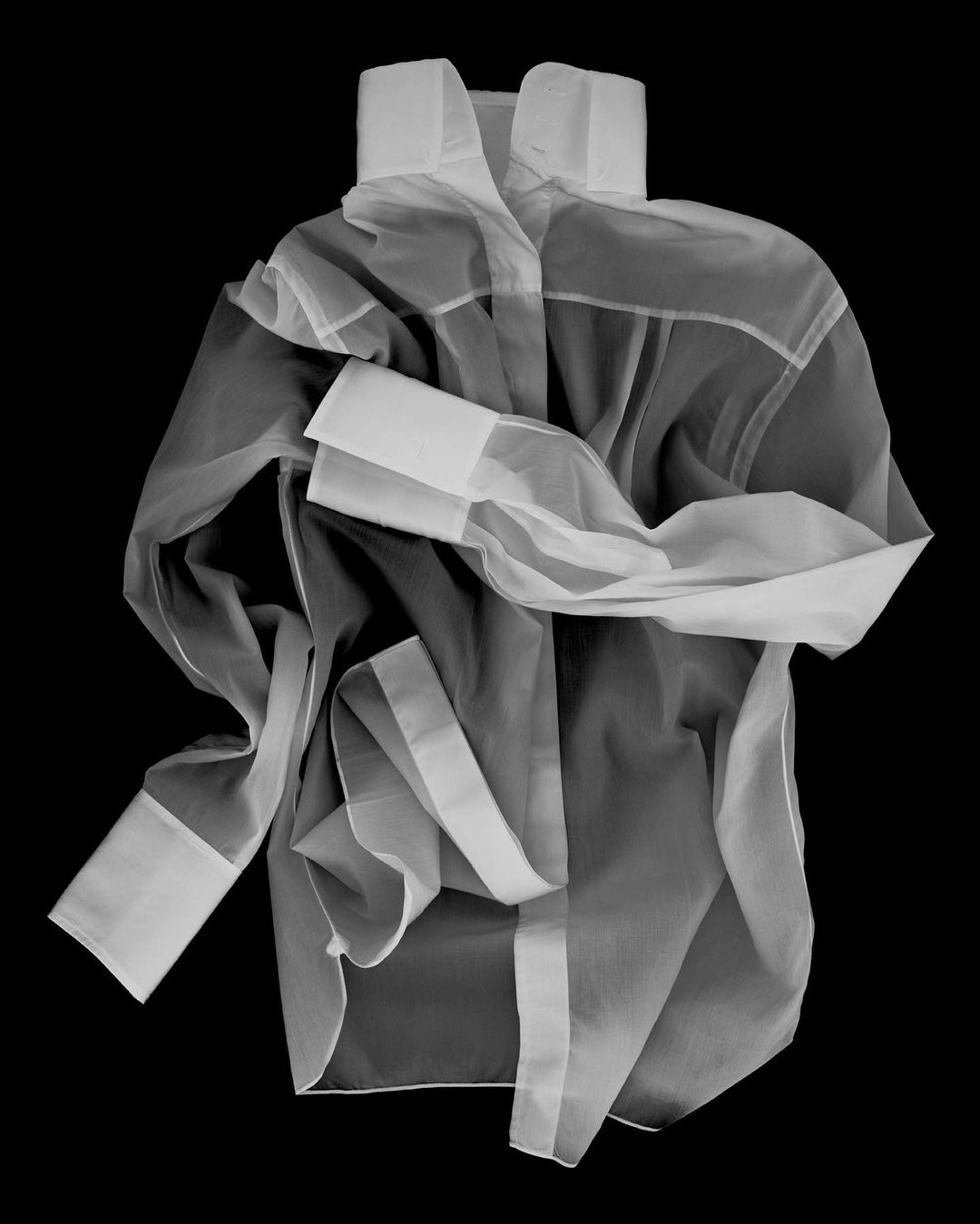 Wrinkled sheer white collared shirt with long sleeves on a black background, showcasing a modern and minimalist fashion item.