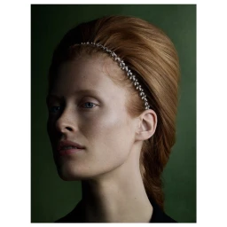 Portrait of a red-haired woman wearing a jeweled headband against a dark green textured background