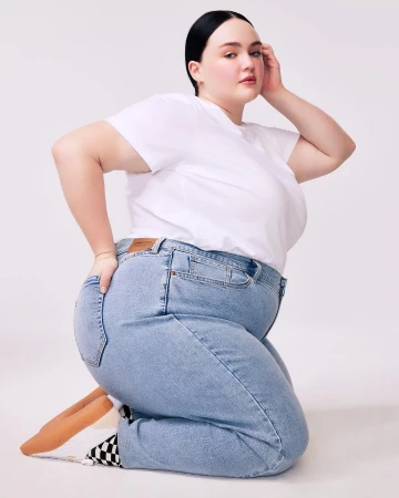 Woman in white t-shirt and jeans kneeling in a studio setting. Fashion portrait showcasing casual style, light blue denim, and simple studio backdrop.