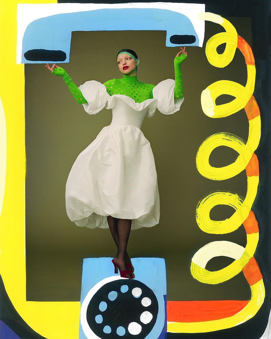 Woman in a white dress with puffy sleeves stands on a blue box with a telephone dial painted on it, against an olive background.