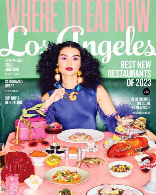 Magazine cover featuring a woman with black curly hair at a table with an assortment of seafood and sushi, with text overlayed.