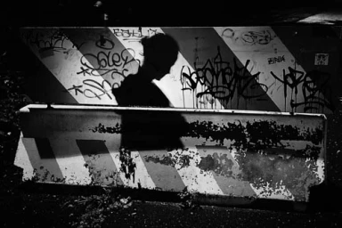 Silhouette of a person walking past a concrete barrier covered in graffiti and striped markings