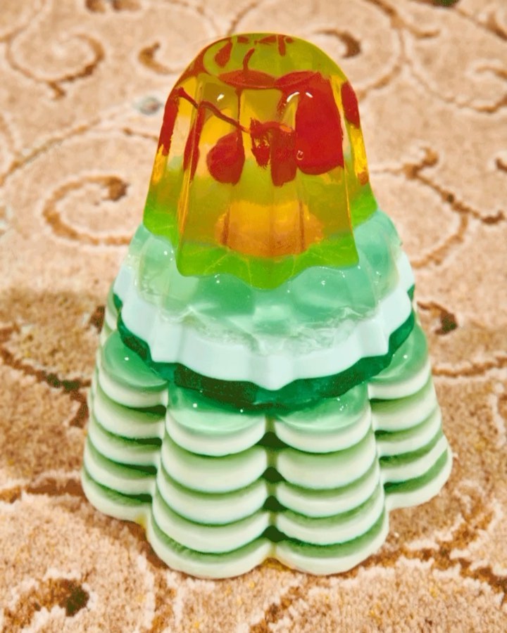 Tower of multi-layered retro gelatin dessert with fruit inside, sitting on a beige patterned surface, in bright studio lighting.