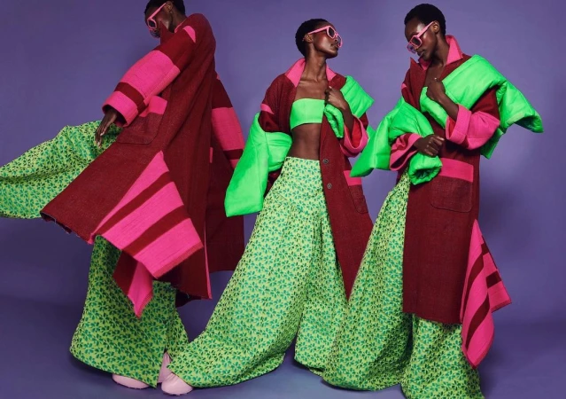 Three identical models in colorful fashion on purple backdrop. Matching coat and pants. Accessories include sunglasses and tube top.