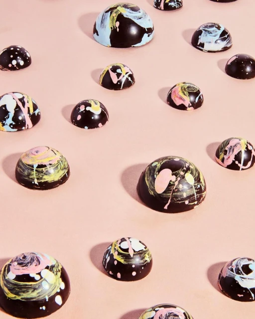 Overhead view of arranged dark chocolate truffles with bright paint splatters on a light pink background. Food and beverage photography.