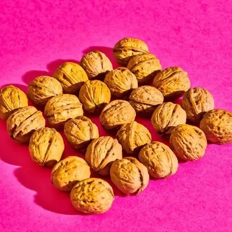 Close-up of a pile of brown walnuts on a vibrant pink background, creating a contrasting and textured food still life.