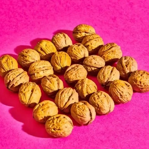 Close-up of a pile of brown walnuts on a vibrant pink background, creating a contrasting and textured food still life.