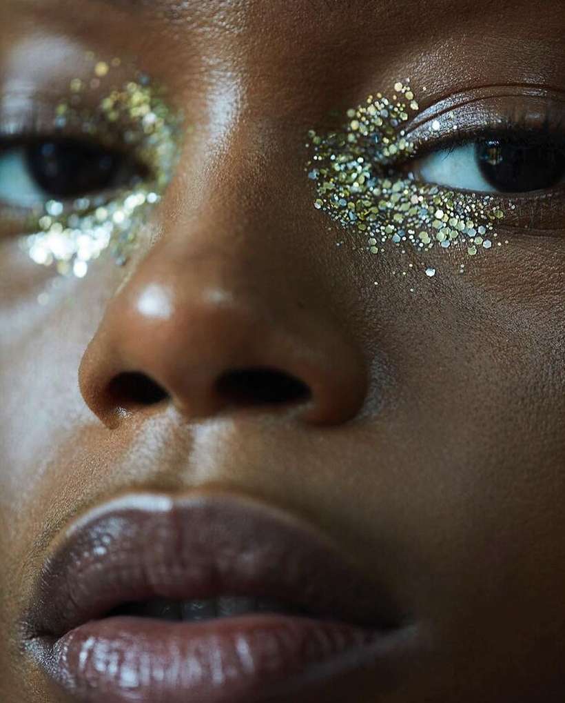 Close-up of a woman's face with gold and silver glitter around her eyes, dark complexion, full lips, beauty shot.