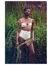 Model with short hair wearing a white bra and high-waisted briefs holding tall grass in a lush green meadow by Julia Kennedy