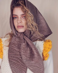 Portrait of a woman wearing a patterned brown headscarf and chunky white knit sweater with yellow trim