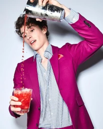 Man wearing a magenta suit pouring red cocktail from shaker into glass by Julia Kennedy