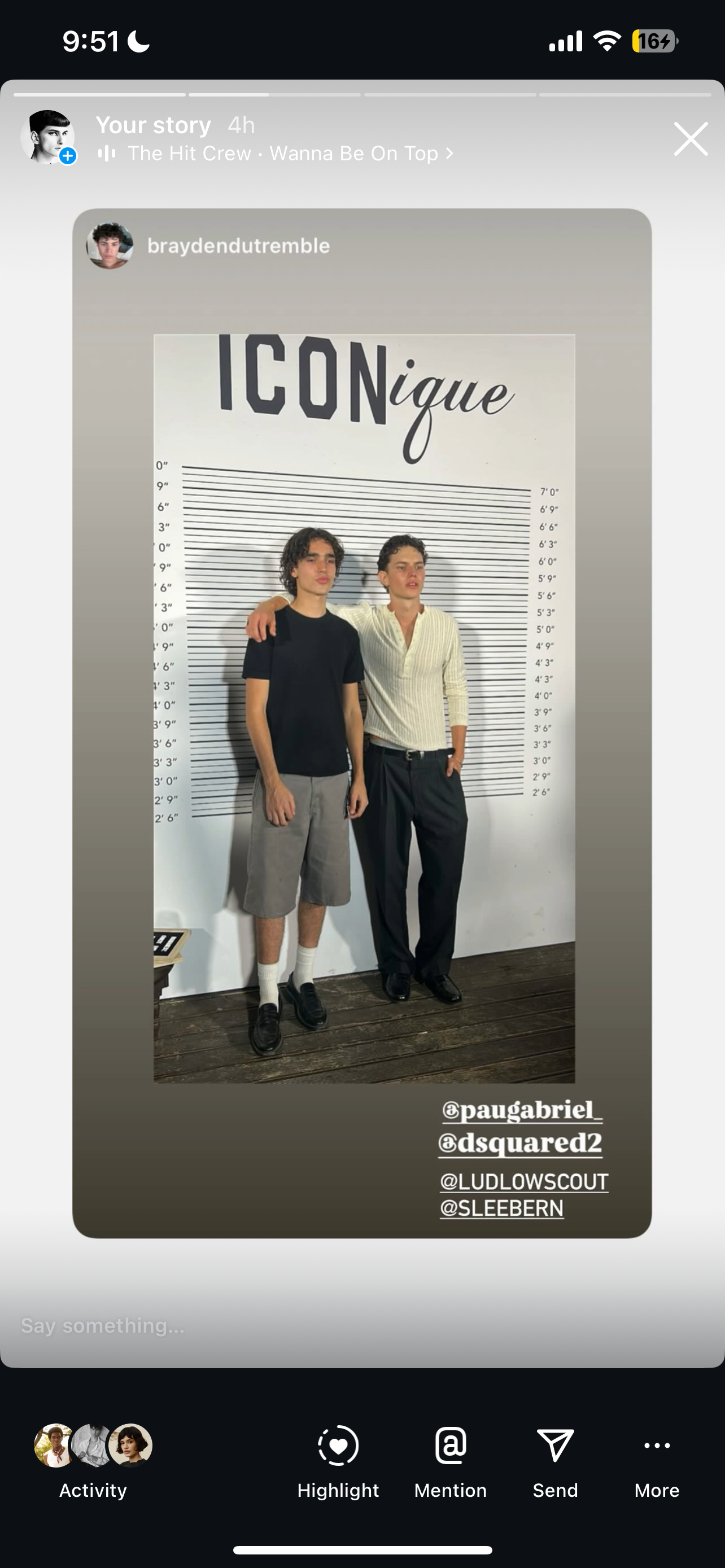 Two men pose in front of a height chart, one with his arm around the other, in a casual indoor photo against a white wall.