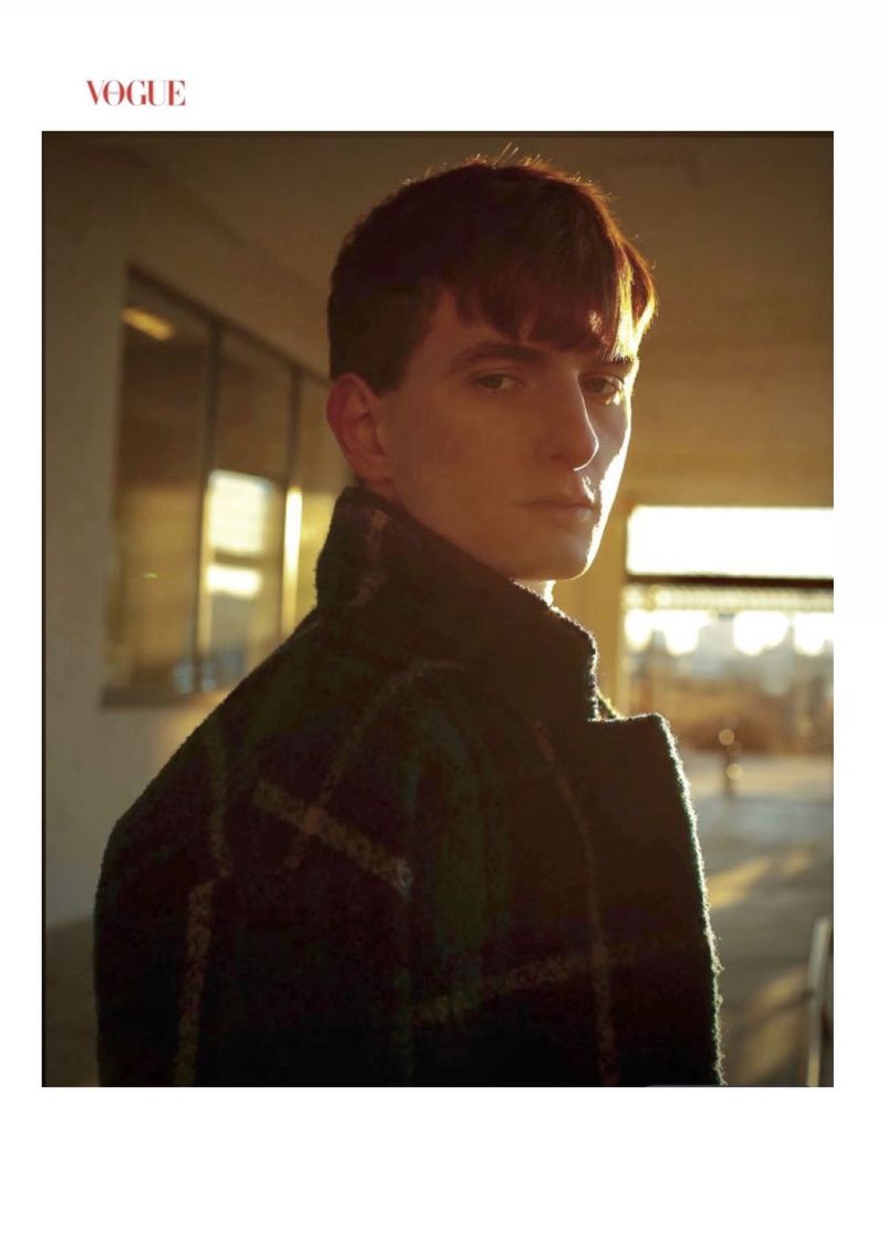 Close-up portrait of a young man wearing a dark plaid coat illuminated by warm golden sunlight outdoors in New York.