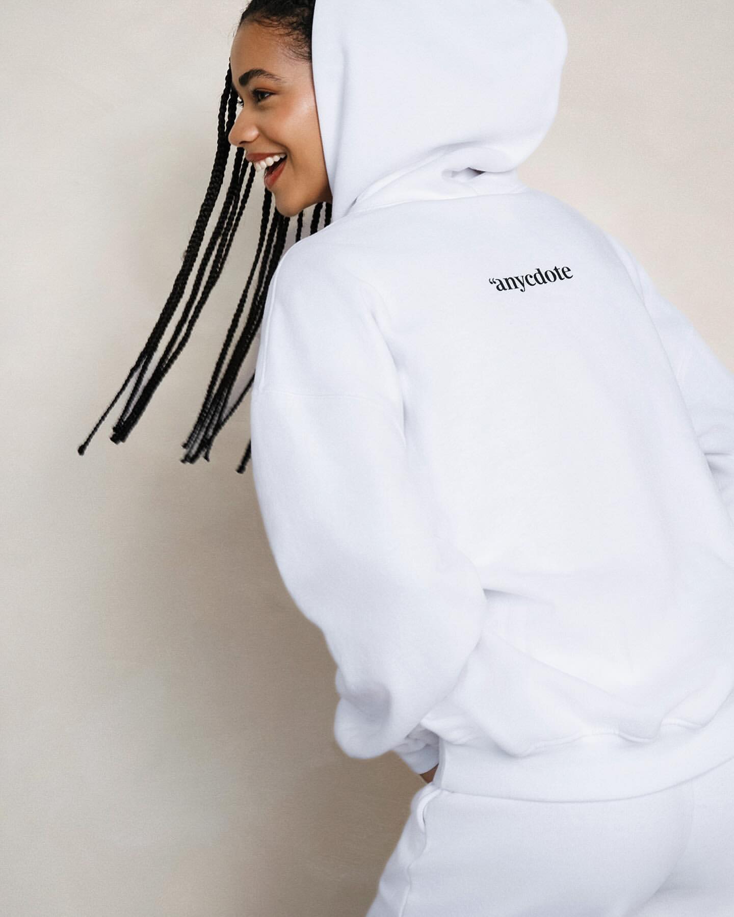 Smiling African American woman wearing a white hoodie and sweatpants in a fashion studio shot against a neutral background.