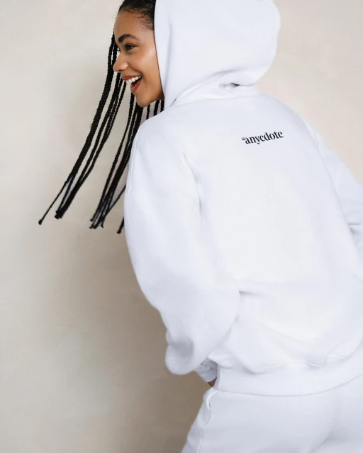 Smiling African American woman wearing a white hoodie and sweatpants in a fashion studio shot against a neutral background.