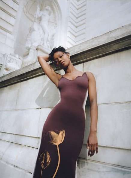 Woman in a brown floral dress poses against a marble wall with an architectural detail featuring a carved sculpture of human figures.